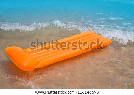 Beach shore with orange floating lounge and waves over sand bottom