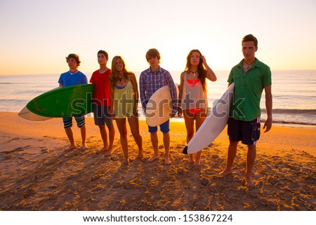 Surfers teen boys and girls group walking on beach at sunshine sunset back light