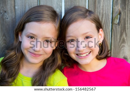 Happy twin sisters with different hairstyle smiling on wood backyard fence