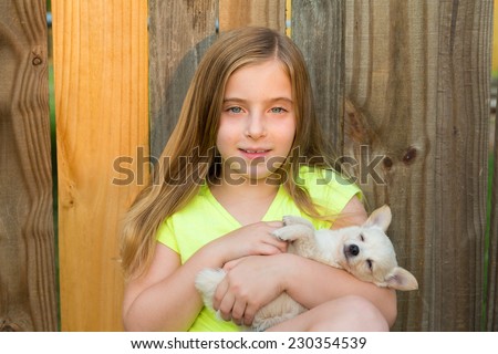 blond kid girl hug a puppy dog happy chihuahua in backyard wooden fence
