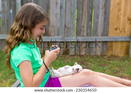 Kid girl taking photos to puppy dog pet with camera in outdoor backyard