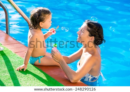 Baby girl blowing soap balloons with mother in swimming pool at summer vacation