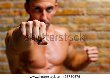 muscle boxer shaped man fist to camera on brick wall