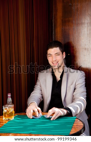 Latin handsome gambler man in table playing poker cards and drinking whisky