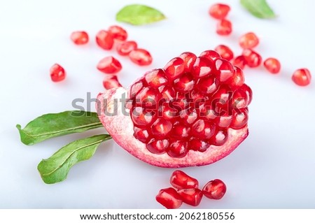 A piece of a beautiful ripe young juicy pomegranate in a beautiful peel with young fresh pomegranate leaves and scattered pomegranate seeds, isolated on a white background