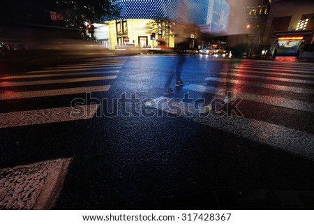 Night view of Crosswalk and pedestrian at modern city zebra crossing street in rainy day. Light trails and Blur abstract.
