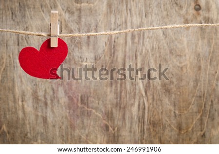 Red fabric heart hanging on the clothesline. On old wood background.