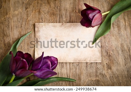 The old card and fresh tulips from two corners is lying on wooden background
