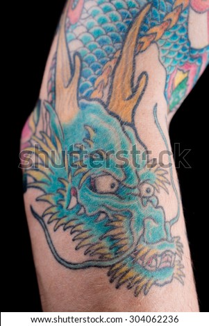 A detailed shot of a blue/green dragon tattoo in Japanese style on the forearm, elbow and bicep of a white male isolated on a black background.