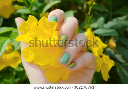Woman hand with sparkle green manicure and yellow flower