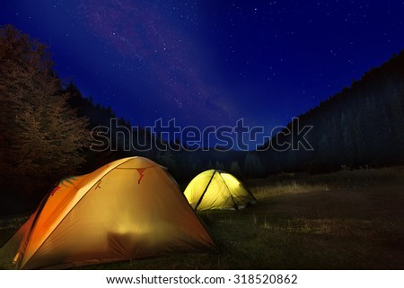 Photo of camp with glowing tents in front of milkyway night sky in the mountains