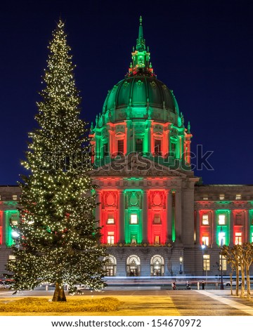 San Francisco City Hall in red and green light and a Christmas tree in front.