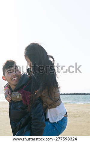 Hispanic and Japanese Couple looking at each other lovingly at the beach wearing jackets and scarfs as the wind blows