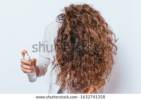 Unrecognizable young woman applying moisturizing spray to her beautiful curly hair, holding her head down. Foto stock © 