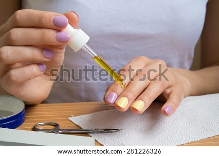 Women\'s hands with bright nail polish is applied oil for cuticles. A girl sitting at a wooden table with manicure tools.