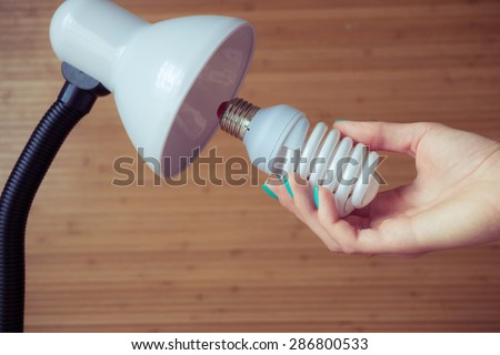 Installation of a modern economical bulb in a table lamp. Female hand holding spiral lamp.