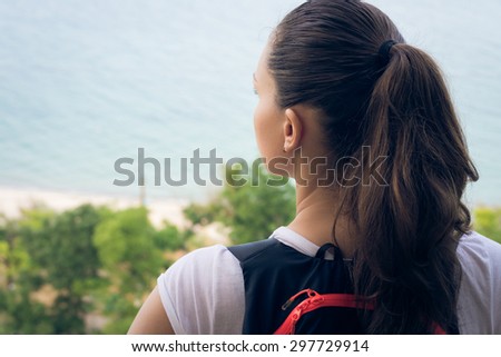 Woman tourist stands on a hilltop on the beach and gazing into the distance. On her back hangs a backpack traveler. Healthy lifestyle in summer outdoors. A trip to the coast.