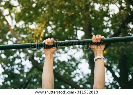 Female hands on the horizontal bar outdoors in the park. Sports activities on fresh air in the summer.