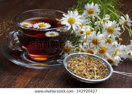 Chamomile tea and dried flowers on wooden table