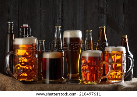 Assortment of beer glasses on table with burlap cloth, dark wooden background
