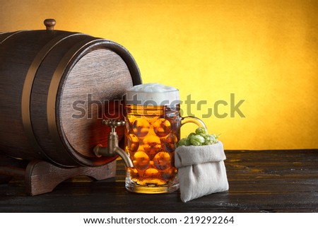 Vintage beer barrel with huge glass of beer and burlap bag with fresh hops on wooden table still life