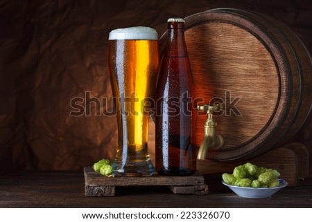 Bottled and unbottled beer glass with barrel and fresh hops for brewing still-life