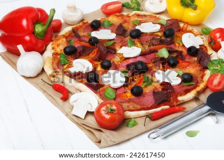 Pizza on white wooden table with tomato, ham, mushrooms, pepper, garlic and olives