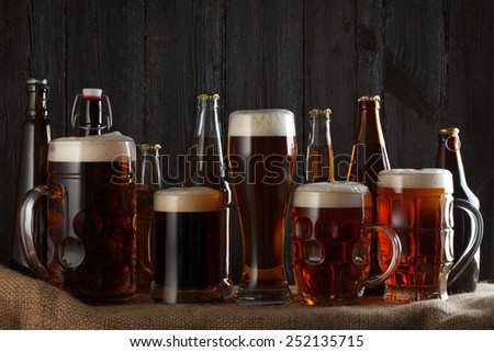 Beer glasses and bottles with lager, dark lager, brown ale, malt and stout beer on table, dark wooden background
