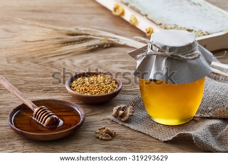 Still life with glass jar full of honey, tee bowl with bee pollen, honeycombs frame, walnuts and rye ears.