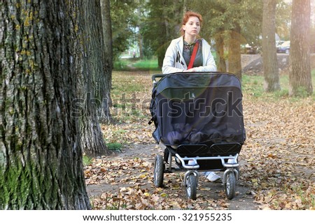 Mom with stroller walks in autumn park alley