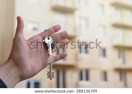 keys to the apartment in his left hand against the background of high-rise buildings