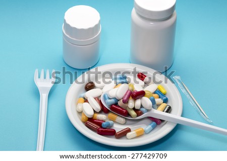 Different pills on a plate with two bottle,spoon and fork on a blue background