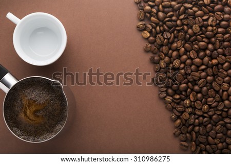 Pot of hot coffee, coffee beans and white empty cup on brown background. Top view. Focus on pot