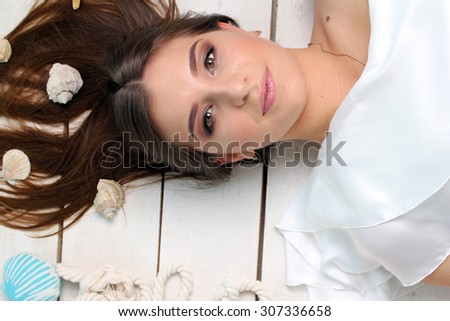 Beautiful girl lying on the floor with seashells in her hair . It looks like a mermaid. Around girl seashells .