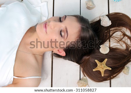 Beautiful girl lying on the floor. Brunette girl , in her hair are shells and starfish .  Lovely girl like a mermaid. The eyes of the girl closed. Portrait . Studio