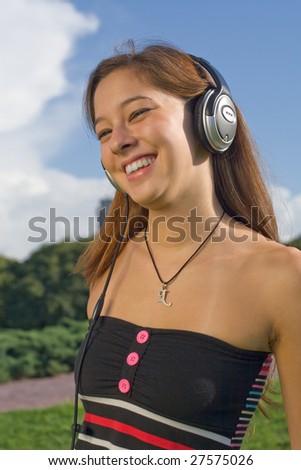 portrait of Beautiful brunette female young woman cute Girl Listening hearing Music with headphones earphones sunny Outdoors green grass blue sky smiling