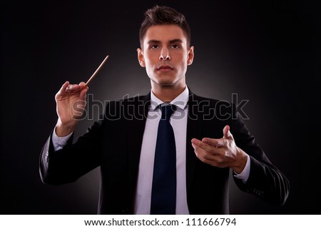 Portrait of a young conductor directing his orchestra. Leadership concept. Young businessman directing with a conductor\'s stick.