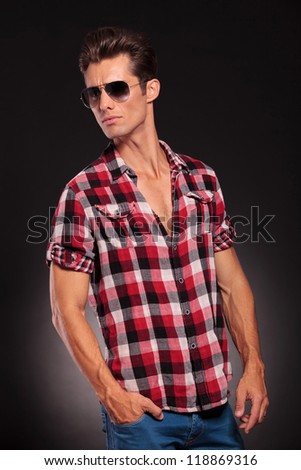 studio side view of a handsome young male model wearing jeans , shirt and sunglasses