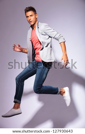 portrait of a jumping casual young man looking at the camera, over light background