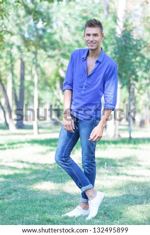 full length portrait of a young casual man posing outdoors with a smile on his face