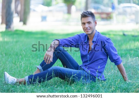 seated young casual man poses in the park with a smile on his face