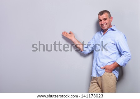 casual senior man presenting something with a hand in his pocket and a smile on his face. on gray background