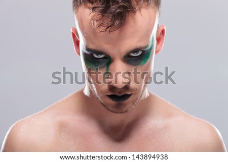 closeup of a casual young man with dramatic makeup looking at the camera without expression. on gray background