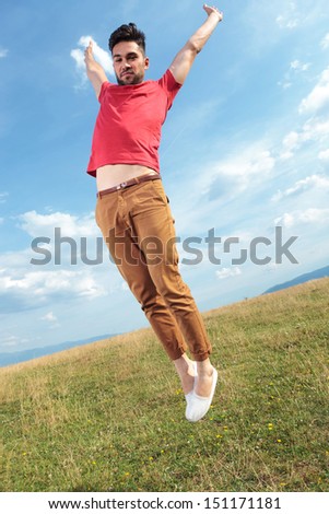 casual young man outdoor jumping with his hands wide open and feet together while looking at the camera