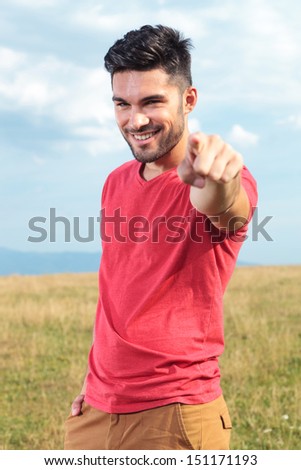 casual young man outdoor pointing at the camera and smiling