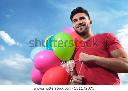 casual young man holding balloons outdoor and looking away from the camera with a smile on his face