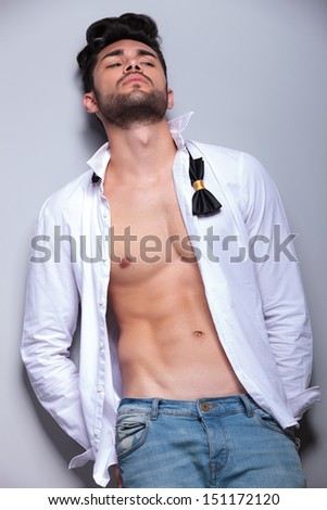 sexy casual young man leaning back and looking away from the camera while holding his hands in his back pockets. on gray background
