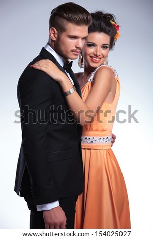 young fashion couple with woman holding her hand on the man\'s shoulder while smiling at the camera. on gray background