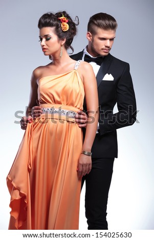 young fashion couple with man behind, looking in opposite directions, away from the camera. on gray background