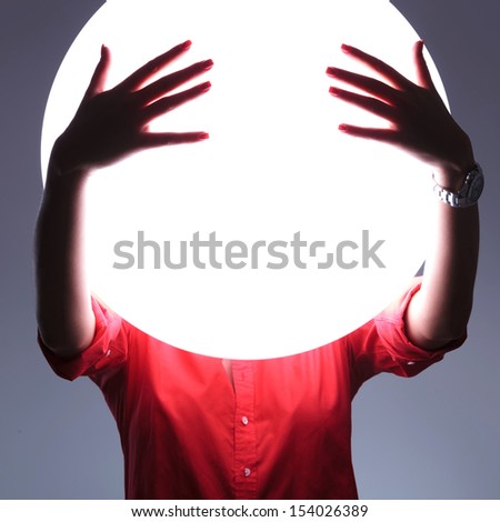 young casual woman covering her eyes over a shiny blank circle. see no evil concept. on gray background